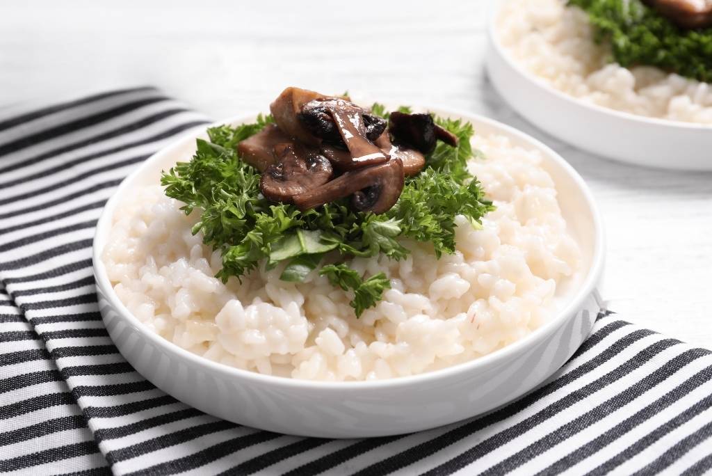 وعاء من الريزوتو الكريمي مزين بالفطر والبقدونس الطازج على مفرش مخطط.