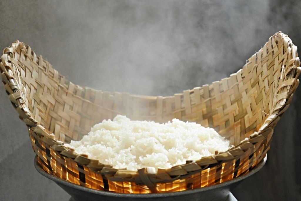 أرز أبيض مطهو على البخار في سلة خيزران تقليدية، مع تصاعد البخار منها.