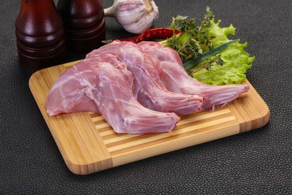 منخفض الصوديوم والكوليسترول ثلاث قطع من لحم الأرنب النيء موضوعة على لوح تقطيع خشبي مع فصوص ثوم وأوراق زعتر.