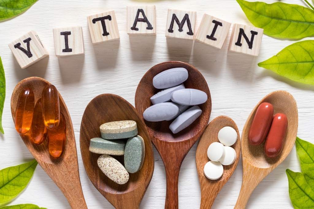 فيتامين B1 (الثيامين) حبوب فيتامينات بأشكال مختلفة في ملاعق خشبية، مع حروف خشبية تُكوّن كلمة VITAMIN.