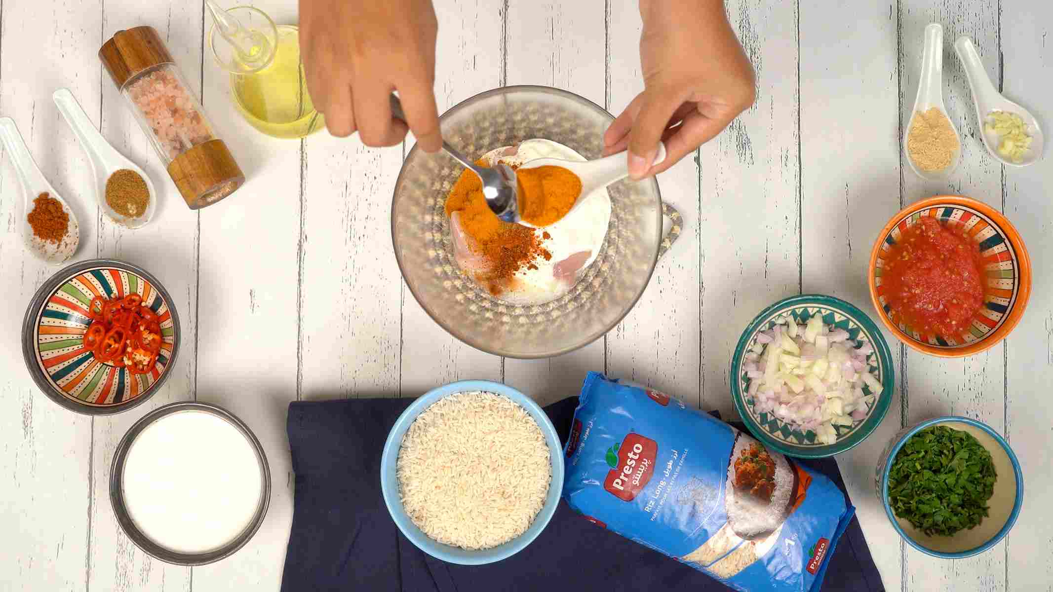 تحضير تتبيلة الدجاج شخص يخلط قطع الدجاج النيئة مع التوابل مثل الكركم والبابريكا واللبن الزبادي في وعاء.