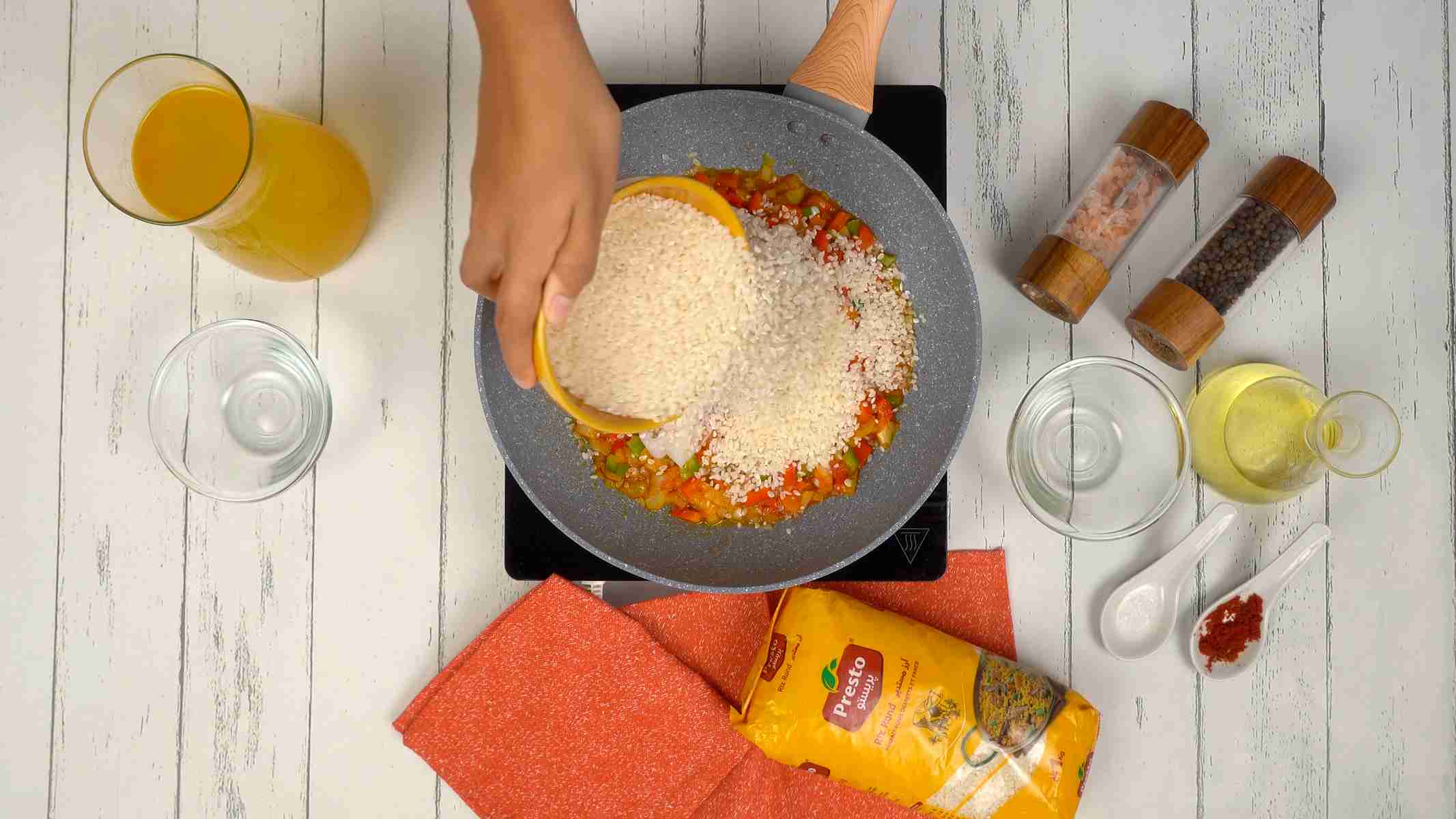 إضافة الأرز شخص يسكب الأرز في المقلاة ويخلطه مع الخضار والمأكولات البحرية.