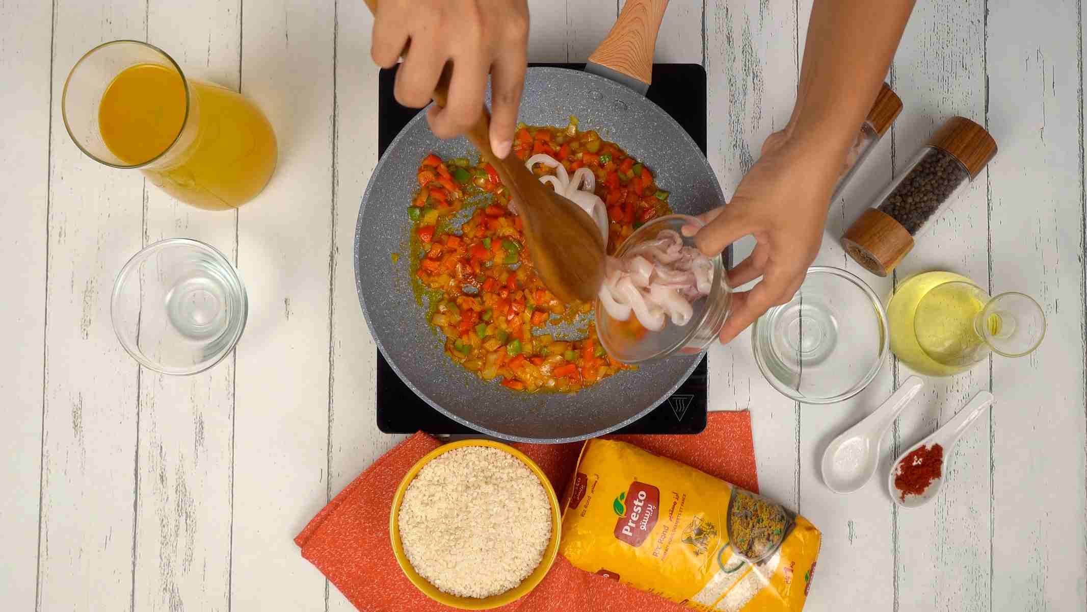 إضافة الكالمار شخص يضيف حلقات من الكالمار النيئ إلى المقلاة مع خضار أخرى.