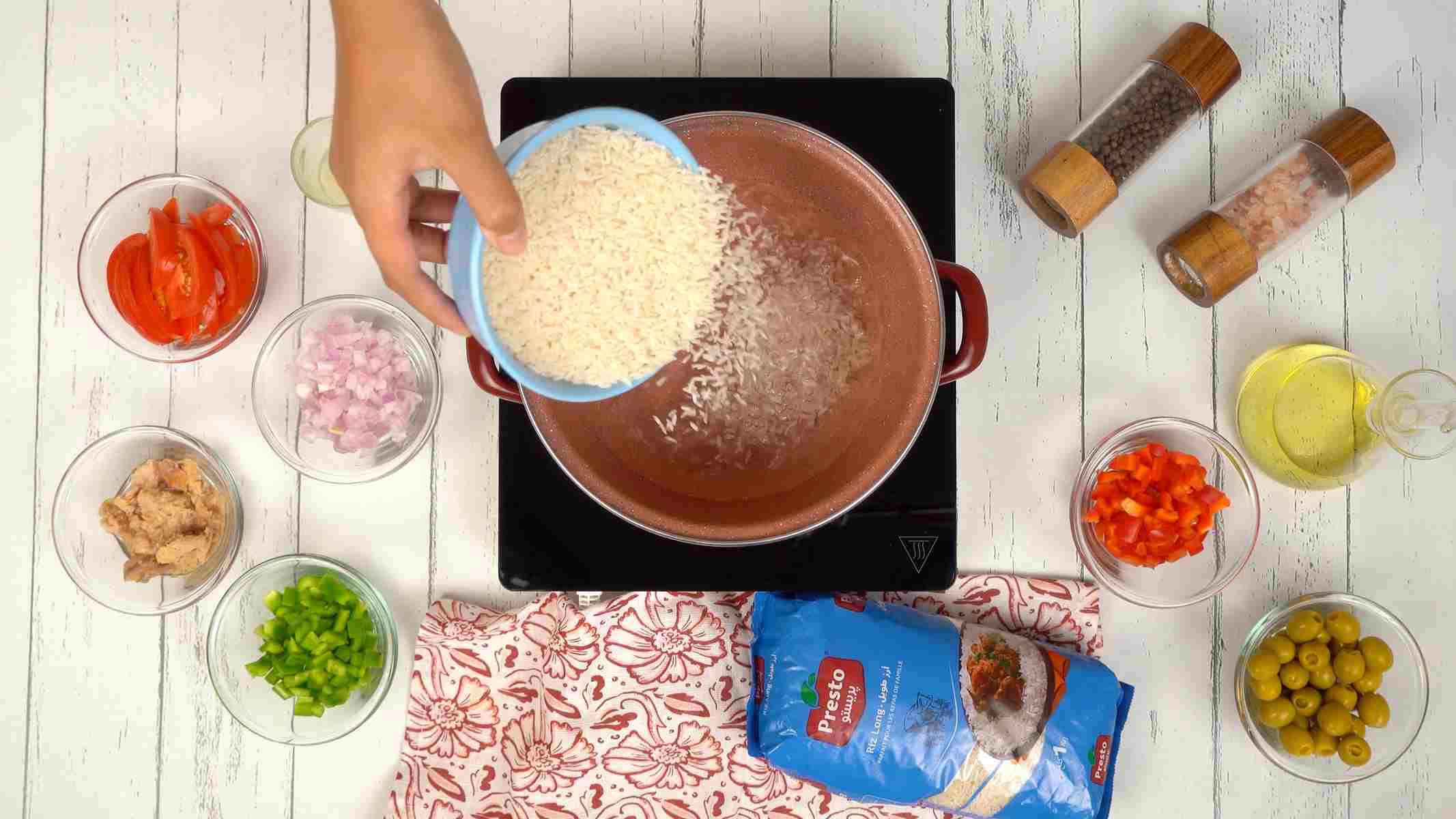 Cuire le riz Une personne verse du riz cru d'un bol bleu dans une casserole d'eau chaude pour le cuire.