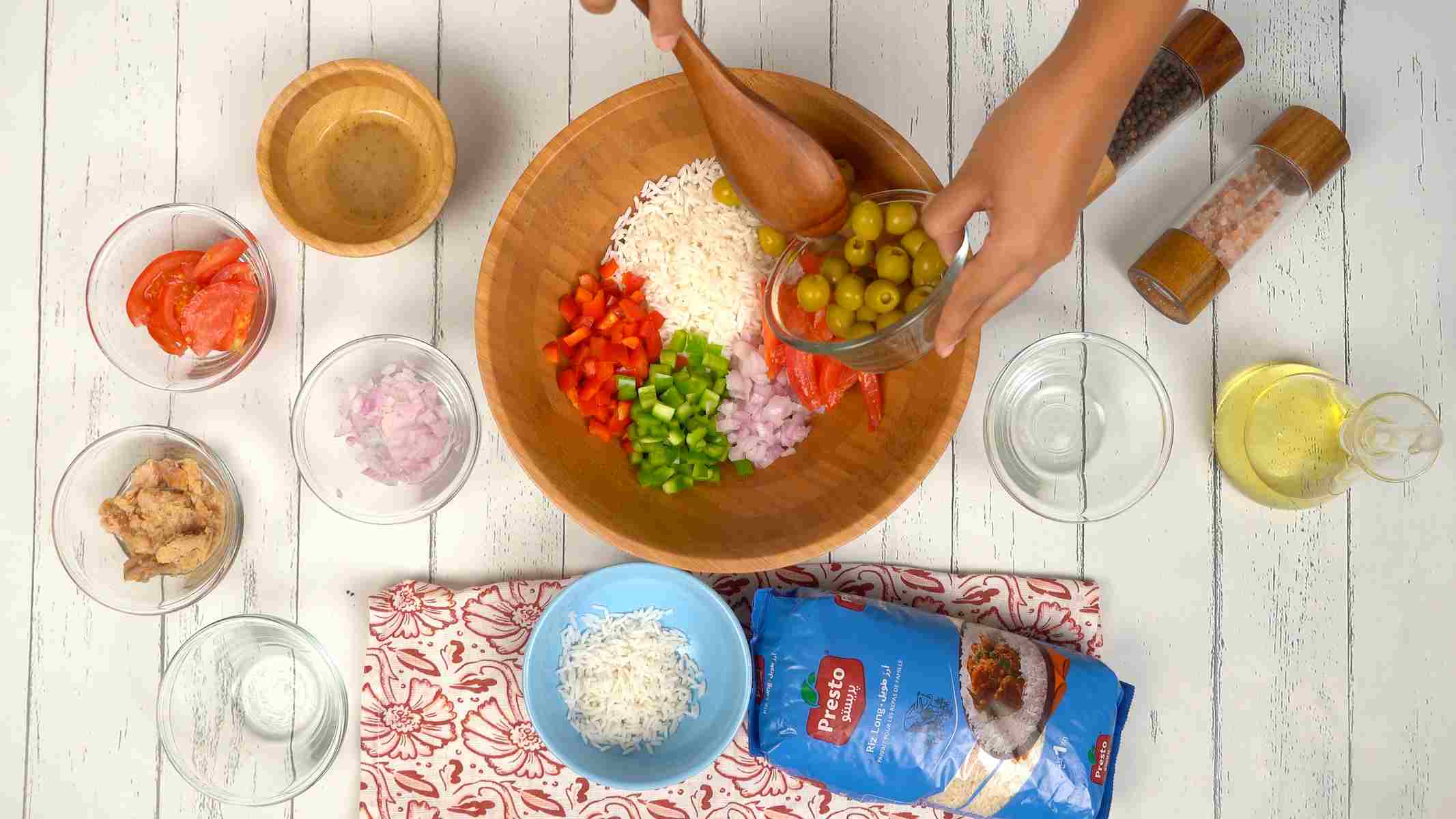 Assembler la salade Une personne ajoute des olives vertes entières dans un grand saladier avec le riz et d'autres légumes coupés.