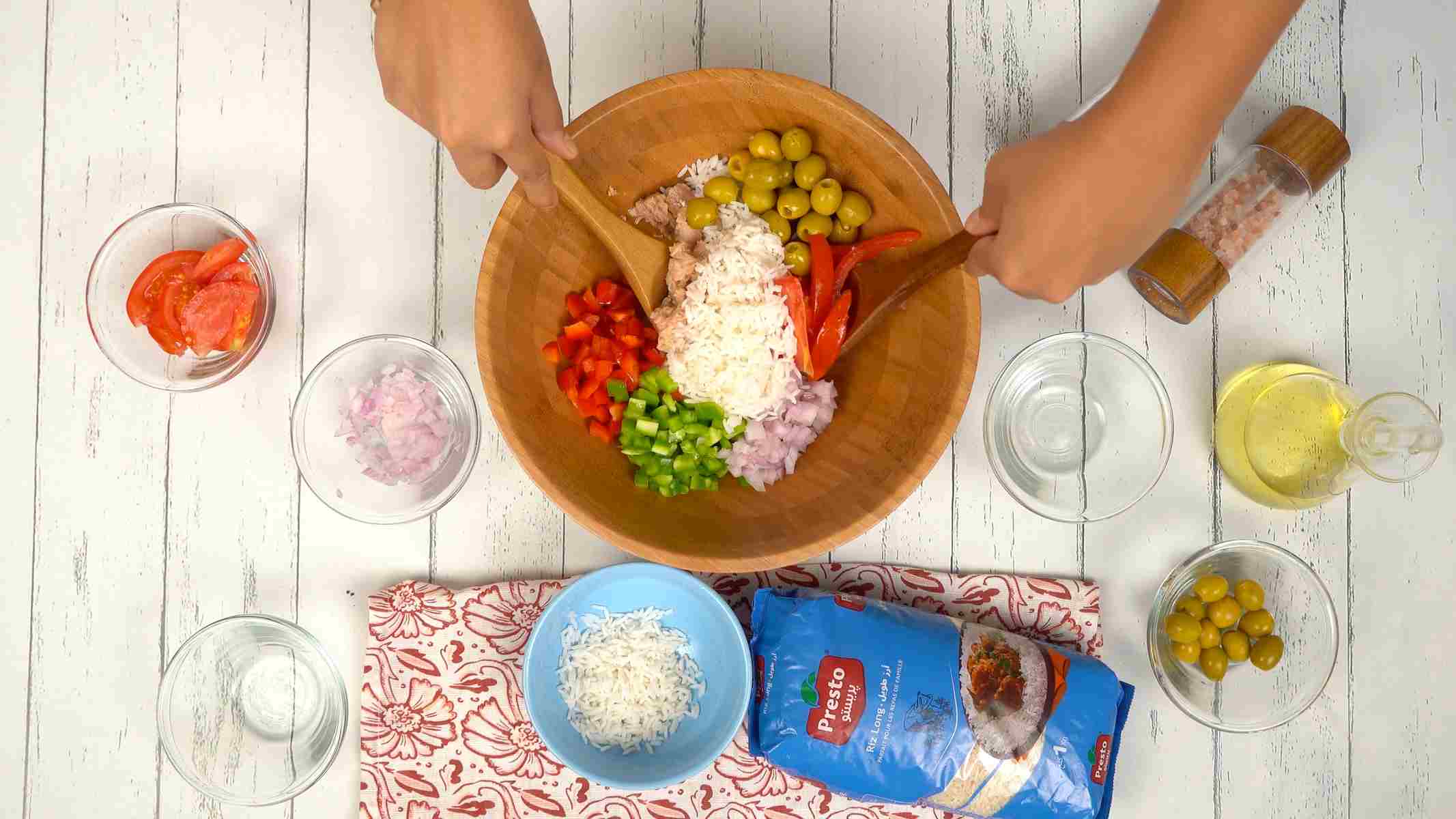 Ajouter la sauce et mélanger Deux mains utilisent des spatules en bois pour mélanger le riz avec du thon émietté et d'autres ingrédients dans le saladier.