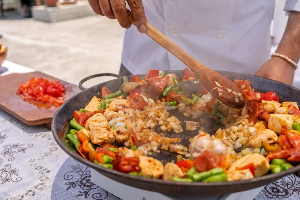 مرحلة من التحضير حيث يقوم طاهٍ بتشويح قطع الدجاج والبصل والفاصوليا الخضراء في المقلاة باستخدام ملعقة خشبية.