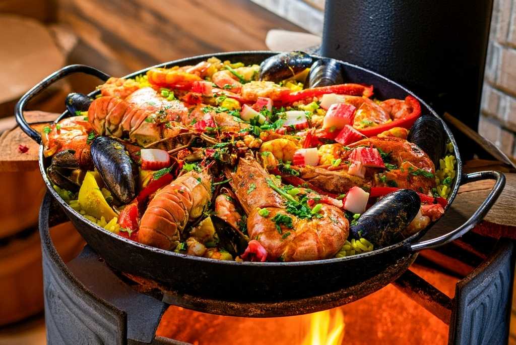 باييلا بالمأكولات البحرية أثناء الطهي، غنية بالألوان، تضم لانغوستين وبلح البحر وفلفلًا أحمر وقطع سرطان البحر.