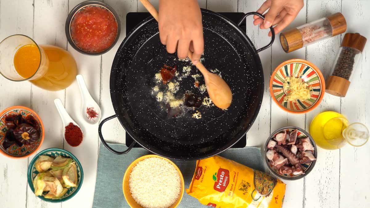 On commence par faire revenir de l'ail haché et des piments séchés dans une poêle à paella avec de l'huile d'olive.