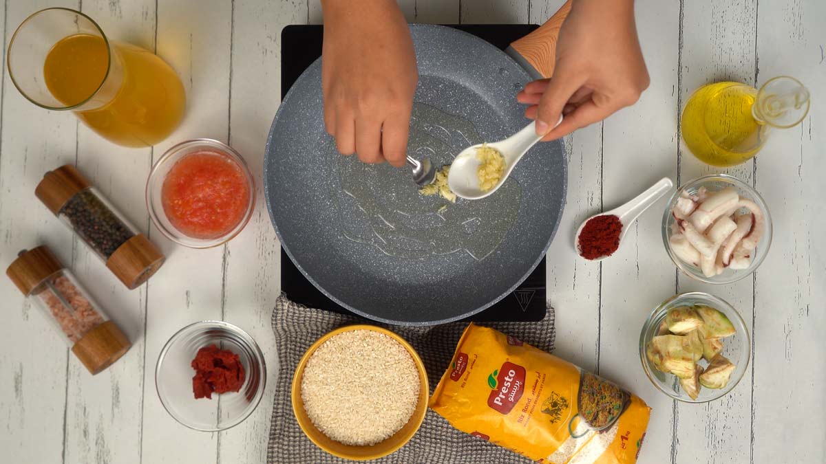 On prépare les ingrédients, notamment le riz rond, des morceaux de poulpe, des cœurs d'artichauts, de la sauce tomate et du bouillon.