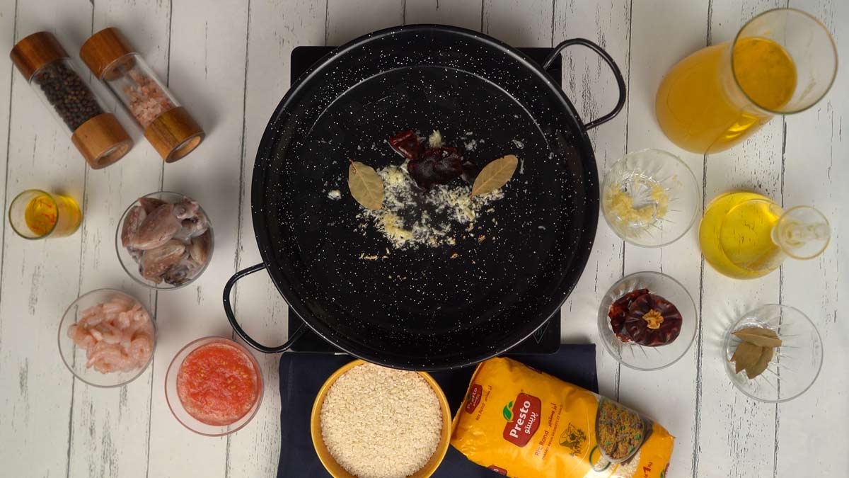 Préparer la base aromatique Dans une poêle à paella noire, on fait revenir l'ail haché, les feuilles de laurier et les piments séchés dans de l'huile d'olive.