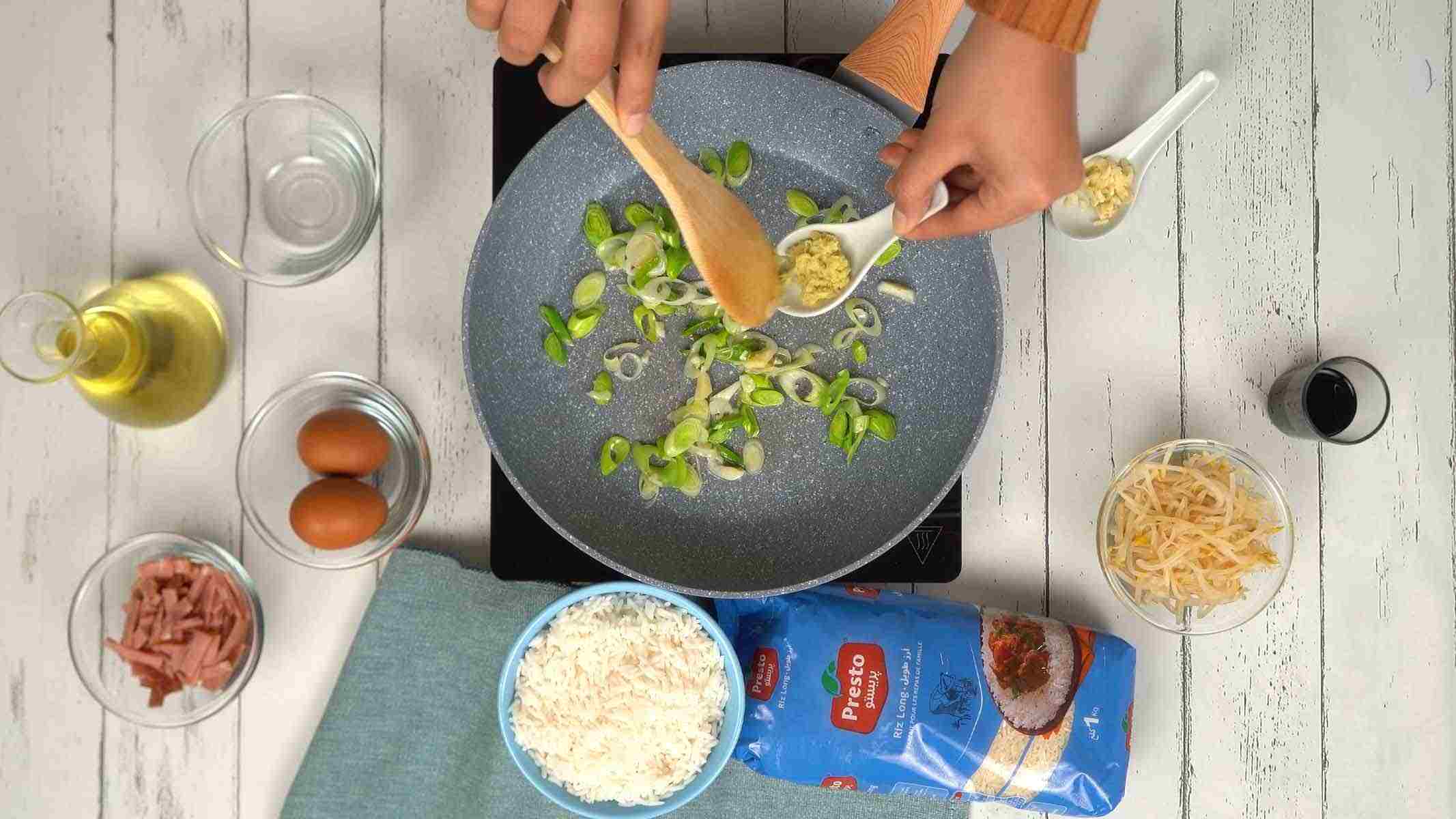 On commence par faire revenir des oignons verts émincés avec du gingembre et de l'ail hachés dans une poêle bien chaude.