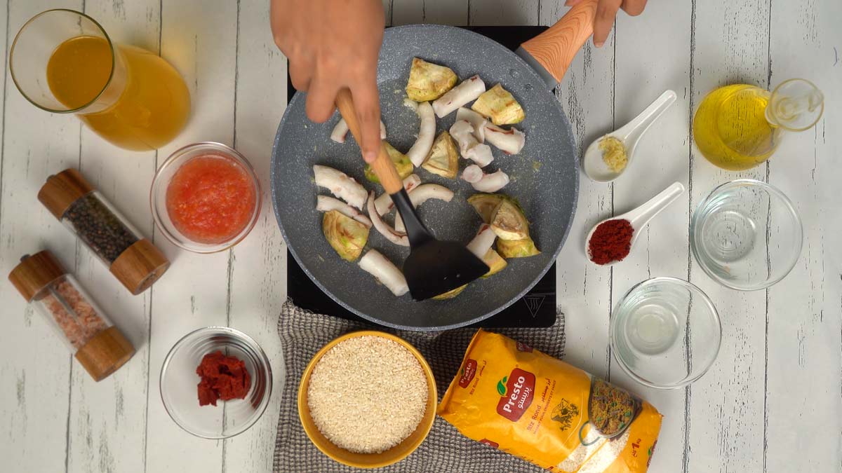 On fait revenir de l'ail haché avec les morceaux de poulpe et les artichauts dans une poêle avec un filet d'huile.