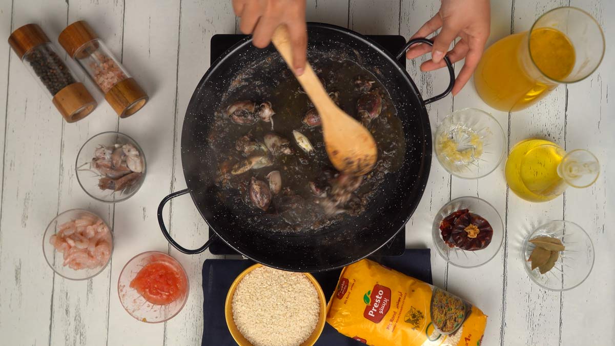 Ajouter la tomate et les calamars On ajoute les calamars entiers pour les saisir. On remarque déjà que le jus de cuisson commence à foncer.