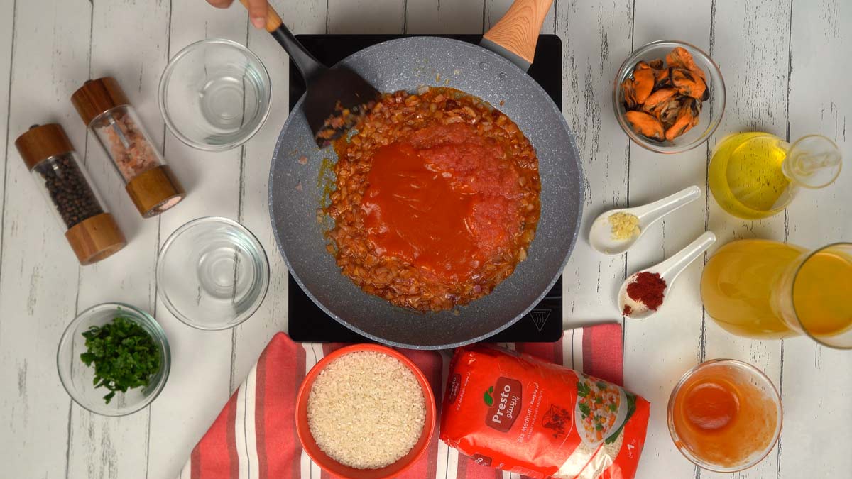 Assaisonner et ajouter la tomate La purée de tomates est ensuite incorporée aux oignons revenus pour créer une base de sauce riche.
