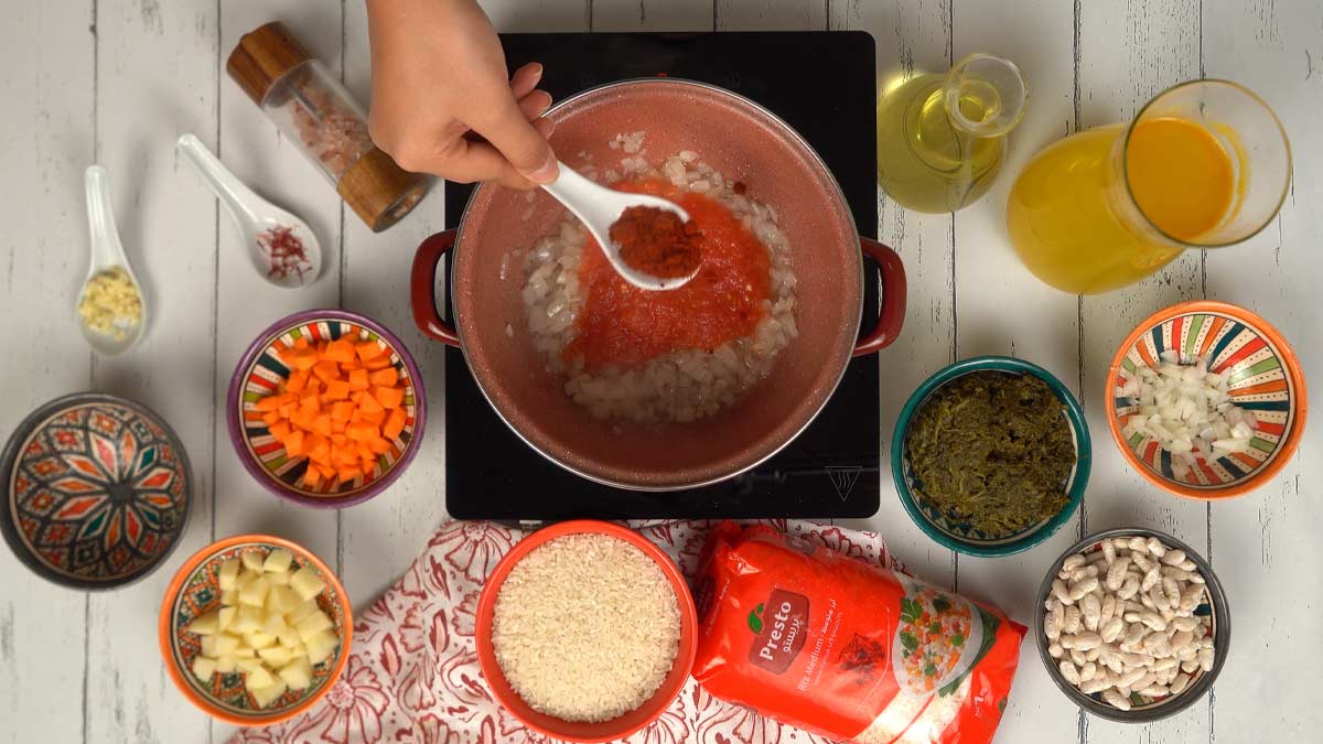 تُضاف الطماطم والتوابل لإعطاء لون ونكهة غنية لقاعدة الطبق.