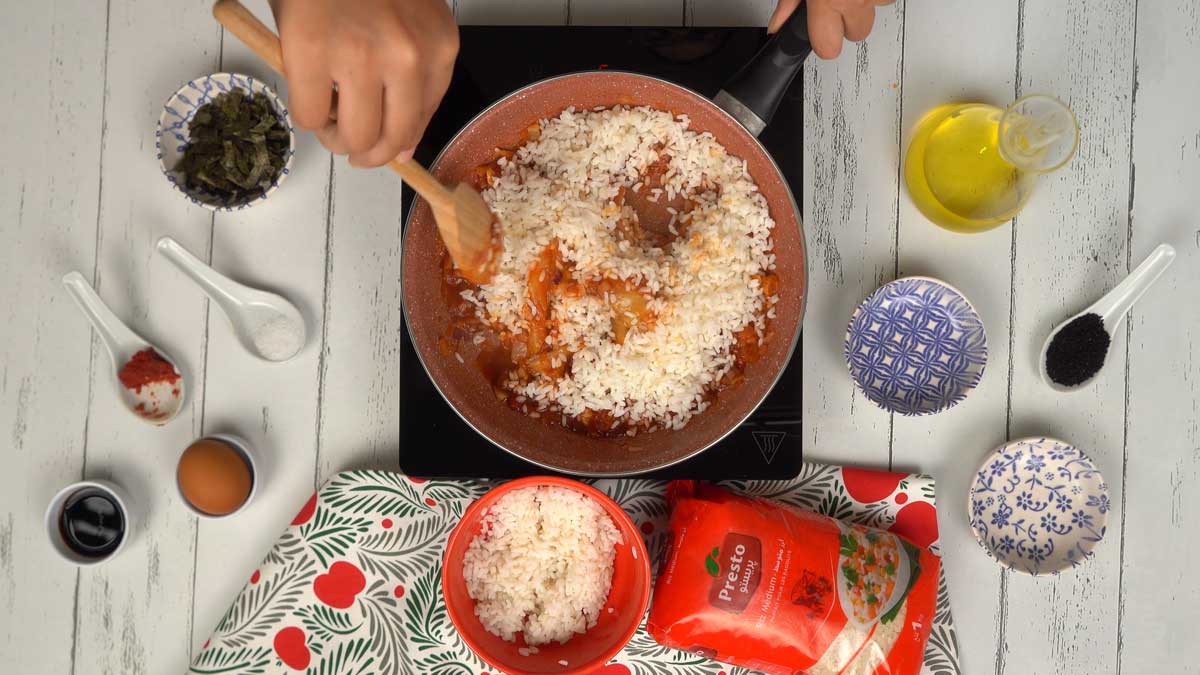 Incorporer le riz On incorpore le riz blanc déjà cuit dans la poêle, en mélangeant bien pour qu'il s'imprègne de la sauce piquante du kimchi.