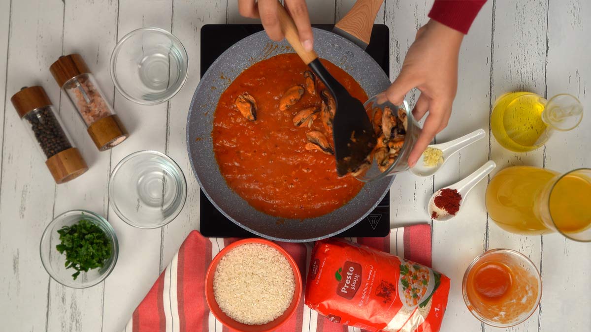 Ajouter les moules Les moules décoquillées sont ajoutées directement dans la sauce tomate bouillonnante.