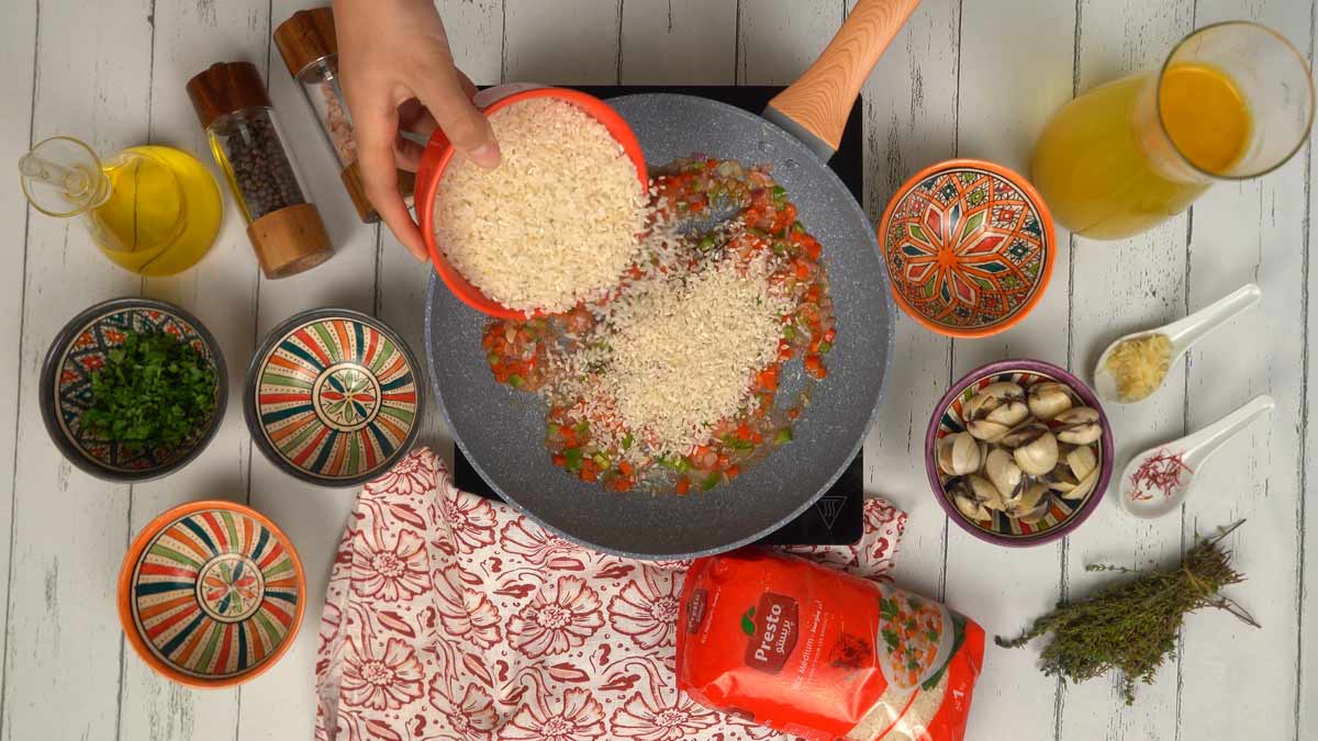 Le riz est versé dans la poêle pour être mélangé aux légumes et absorber les premières saveurs.