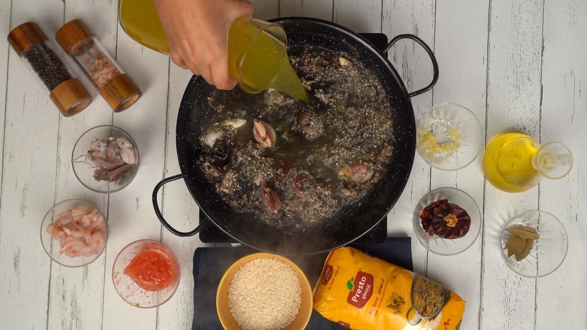 Cuisson au bouillon Le bouillon de poisson est versé sur le mélange de riz et de calamars. C'est à ce moment que l'encre colore l'ensemble de la préparation.