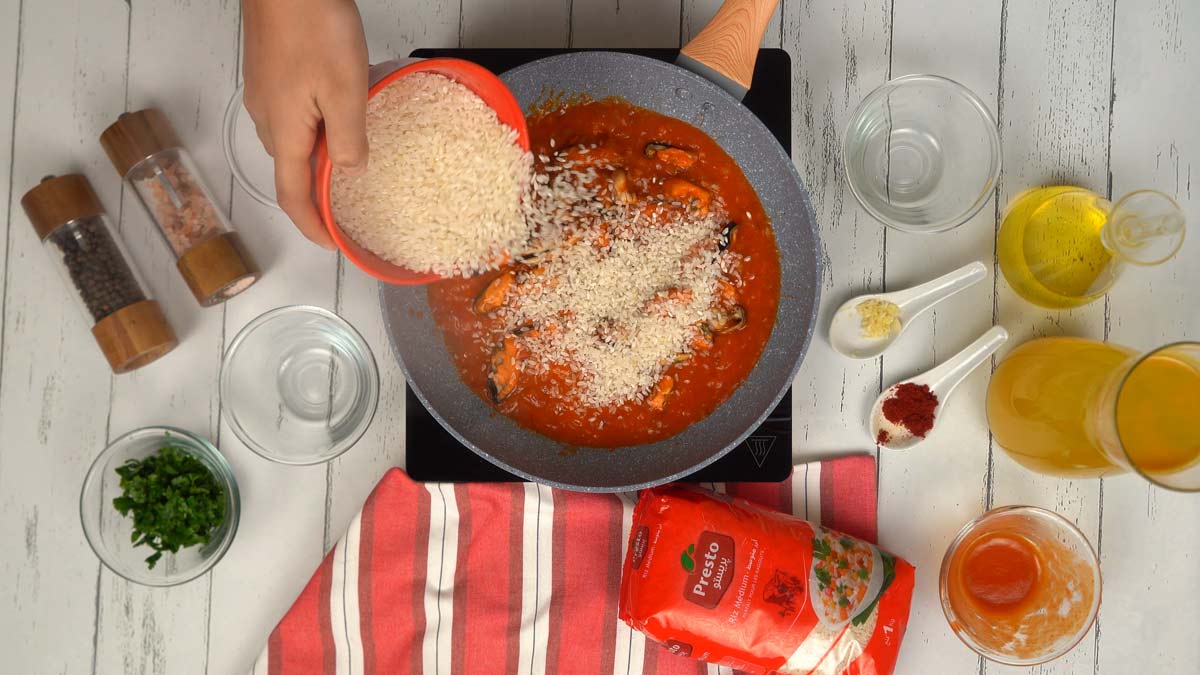 Incorporer le riz Le riz est versé dans la poêle avec les moules et la sauce pour absorber toutes les saveurs, puis mouillé avec le bouillon.
