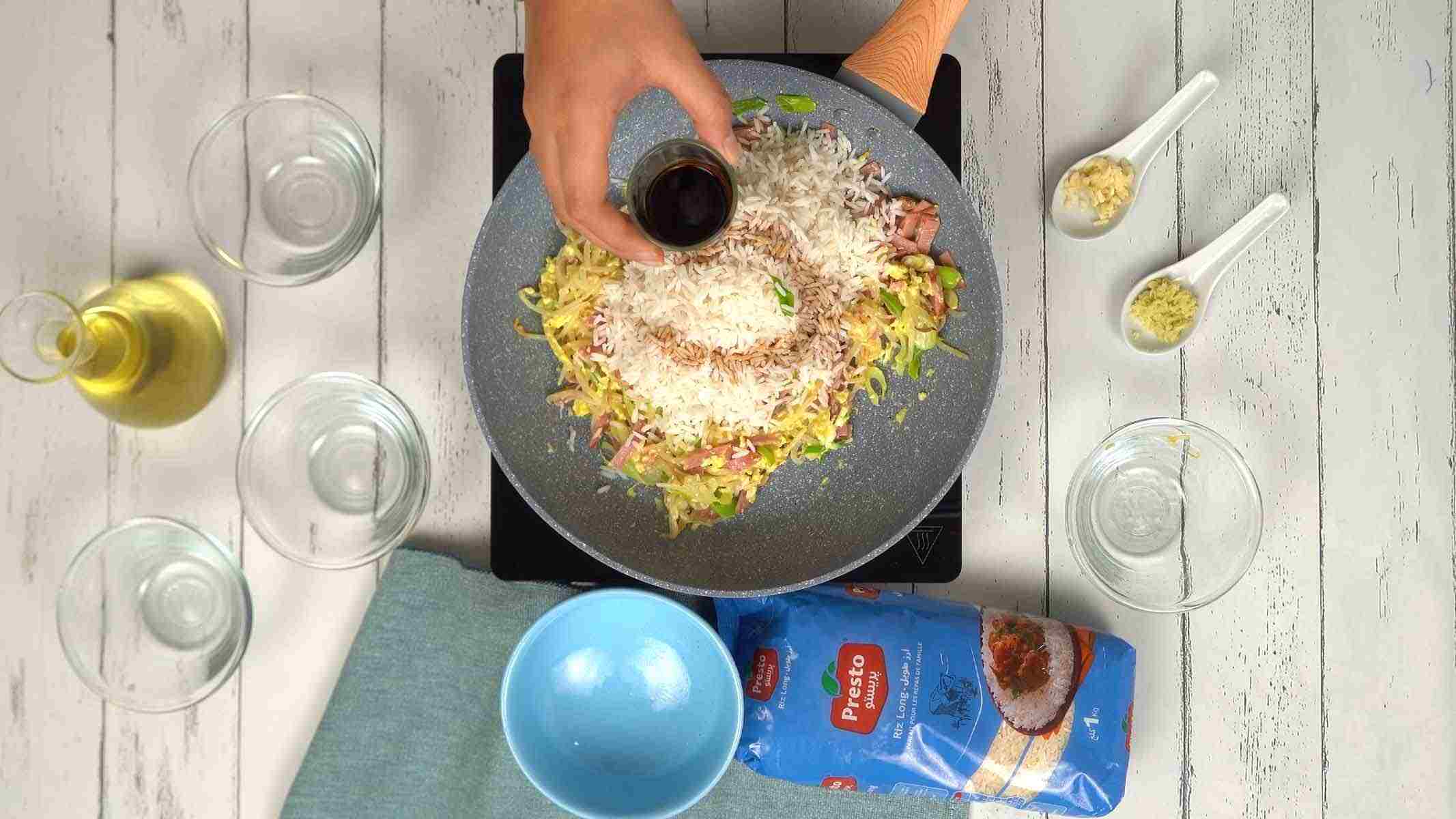 On incorpore le riz long grain cuit et on verse un filet de sauce soja pour colorer et assaisonner l'ensemble.