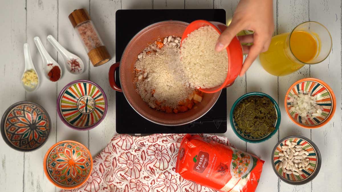 يُضاف الأرز النيّئ إلى القدر ليمتص النكهات قبل الطهي.