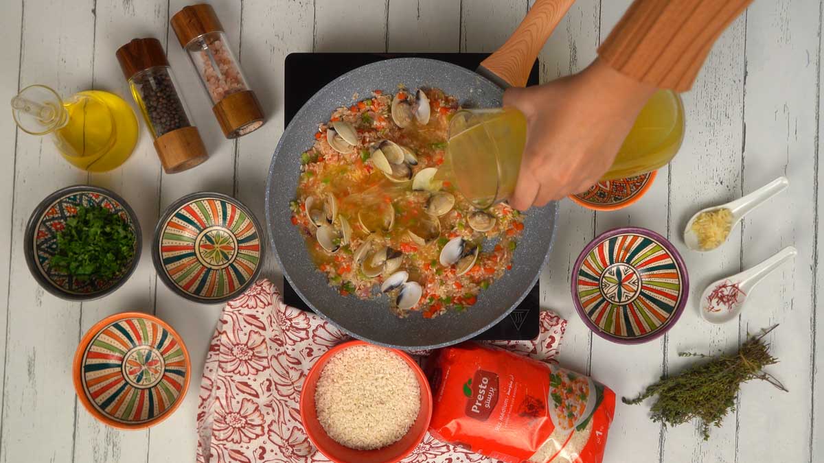 Le bouillon doré est versé sur l'ensemble de la préparation pour permettre au riz de cuire et aux palourdes de s'ouvrir.