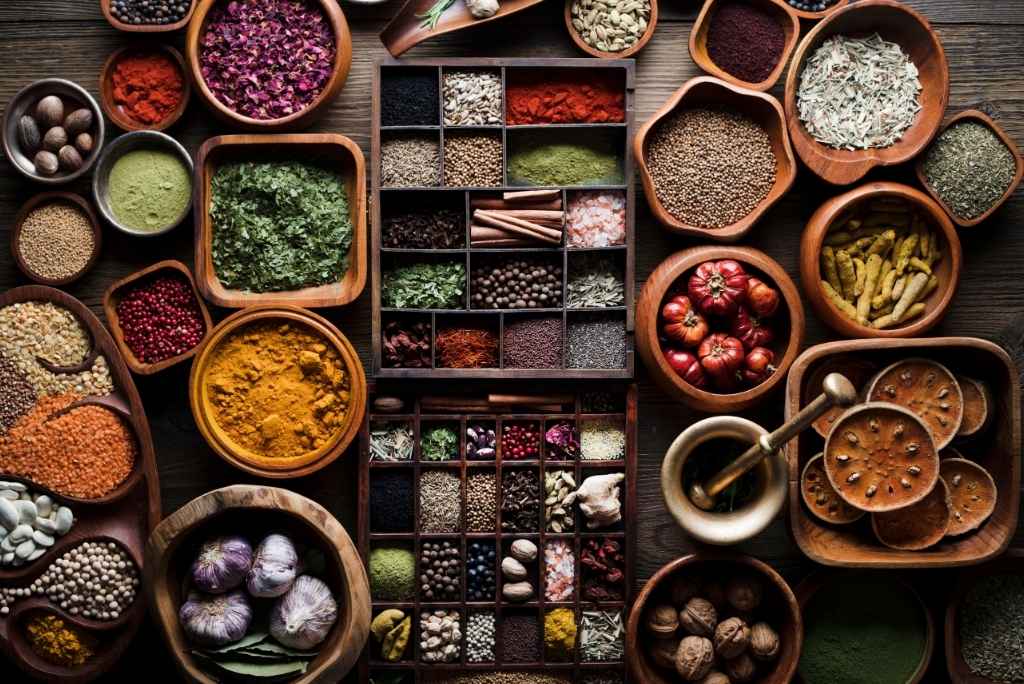 التوابل التي تمنح الأرز الأبيض نكهة مميزة لقطة علوية مذهلة لمجموعة من توابل العالم مرتبة بعناية داخل صناديق مقسمة وأوعية خشبية، مع هاون ومدقة تقليديين.