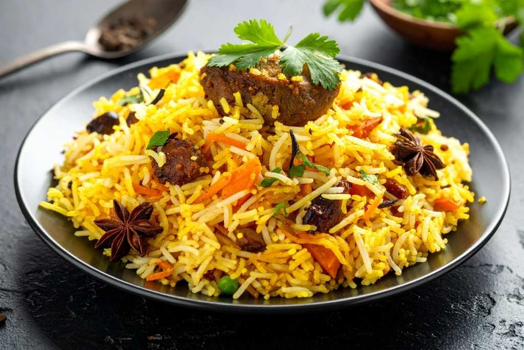 تحميص التوابل قليلًا طبق شهي من برياني أرز البسمتي الأصفر بالزعفران، مزين بقطع اللحم والجزر والزبيب، مع نجمة اليانسون وأوراق الكزبرة الطازجة.
