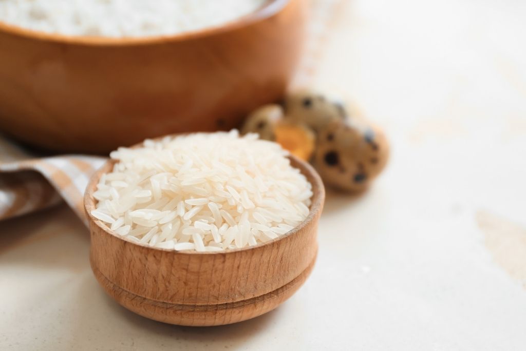 Le riz est naturellement exempt de gluten Un petit bol en bois rempli de riz blanc à long grain, avec en arrière-plan des œufs de caille et un plus grand récipient en bois.