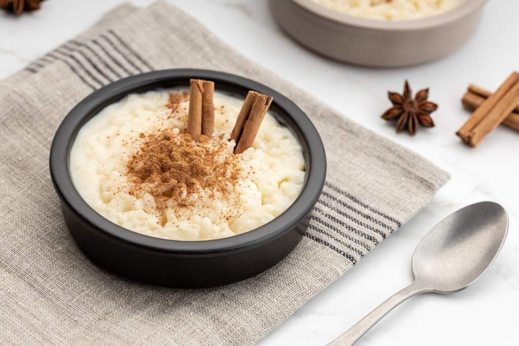 وعاء أسود أنيق يحتوي على أرز بالحليب الكريمي مرشوش بسخاء بالقرفة ومزين بعودين كاملين من القرفة.