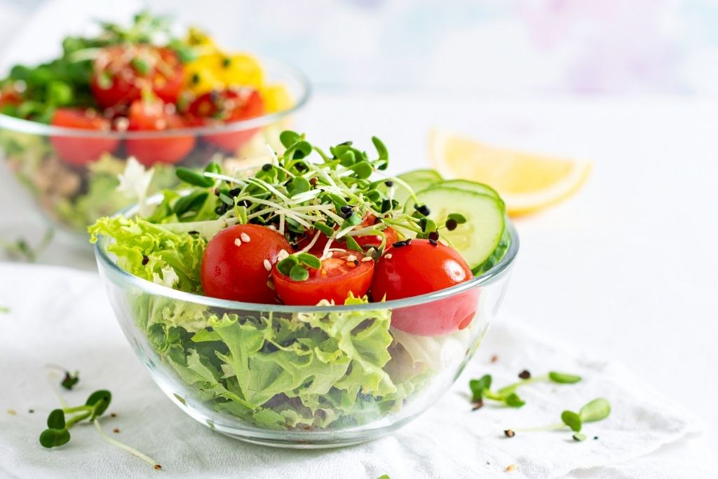 Un bol en verre rempli de laitue frisée, de tomates cerises et de jeunes pousses croquantes parsemées de graines de sésame.