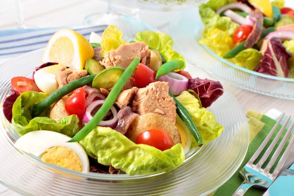 Une salade Niçoise gourmande composée de morceaux de thon, d'œufs durs, de haricots verts, de tomates et d'oignons rouges.